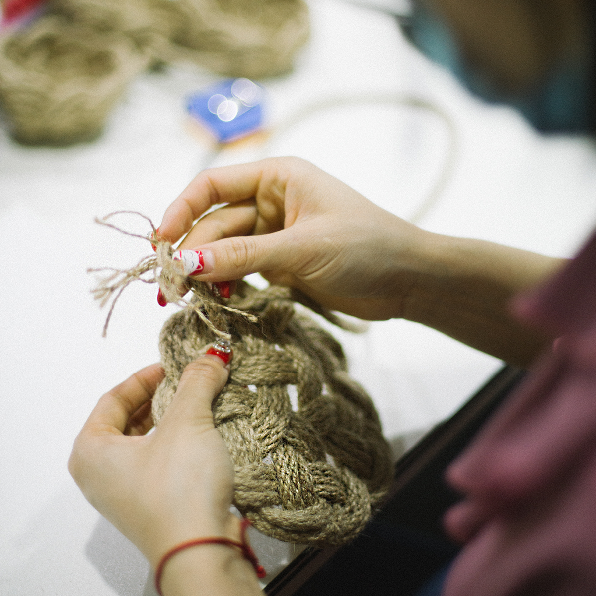 Hands braiding thick natural jute rope on a table, close-up craft activity