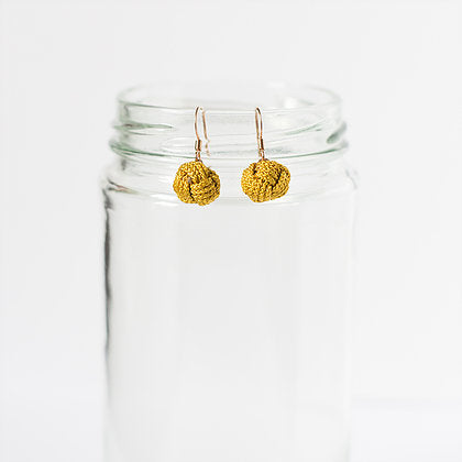 Gold textured dangle earrings displayed on a clear glass jar against a white background